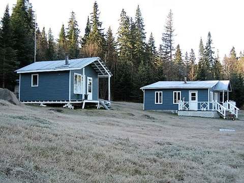Deux chalets en bois situés dans une clairière bordée d'arbres.