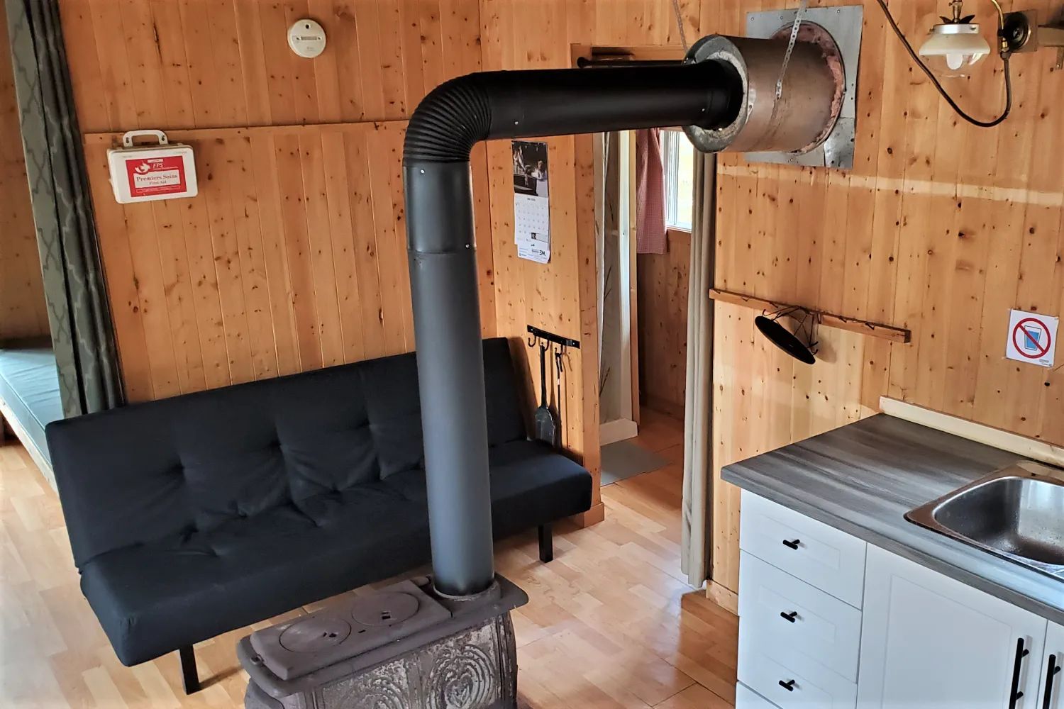L'intérieur du chalet comprend un poêle à bois, un canapé-lit et un coin cuisine.
