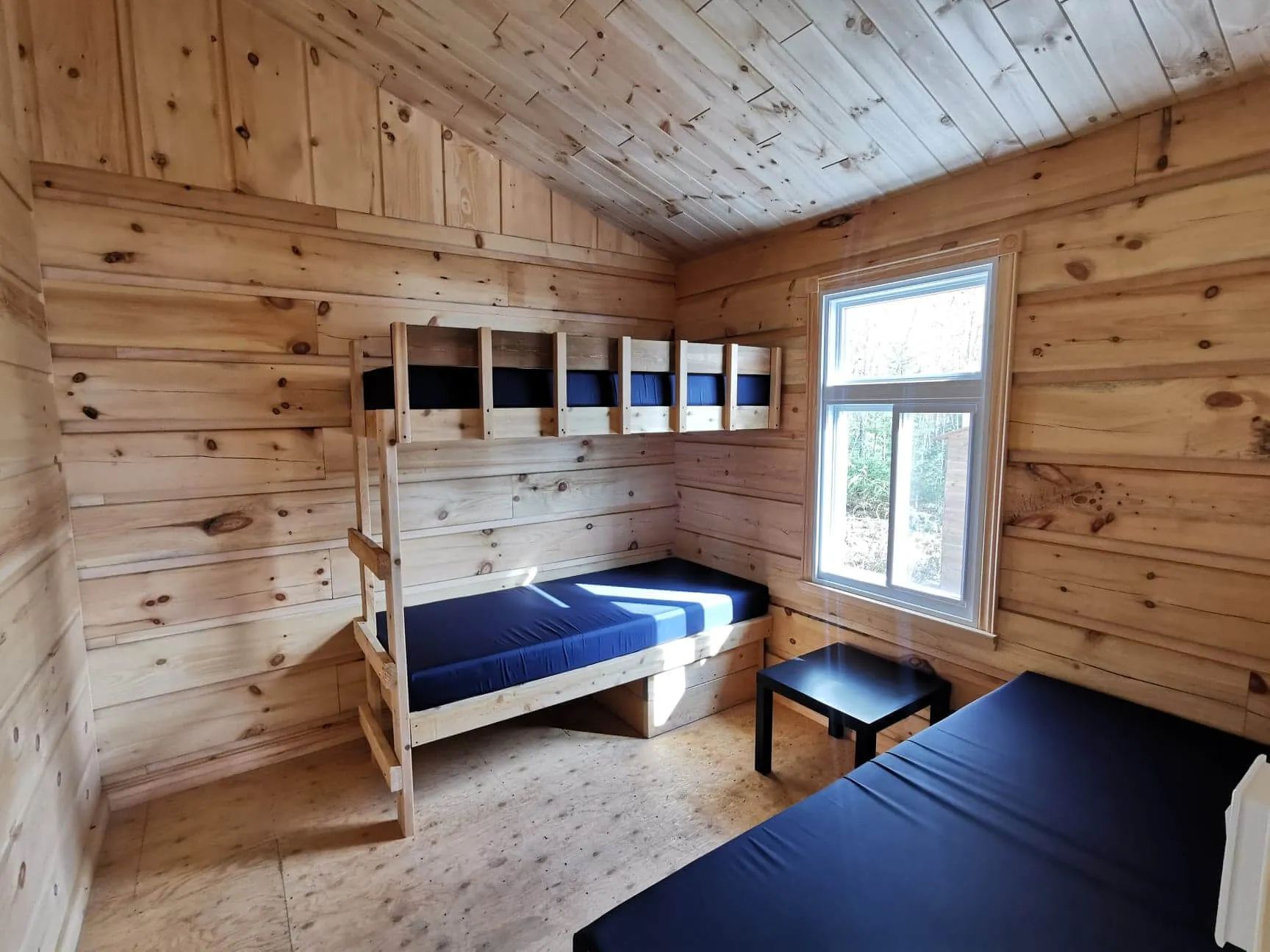 Cette chambre de chalet comprend un lit superposé et un lit simple avec vue sur la forêt.