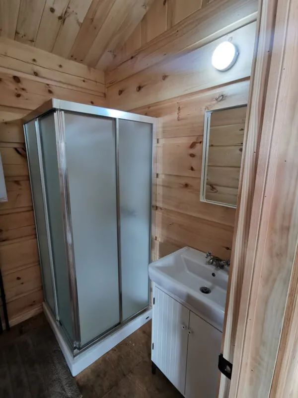 La salle de bain du chalet comprend une douche fermée, un lavabo et un miroir sur des murs en bois.