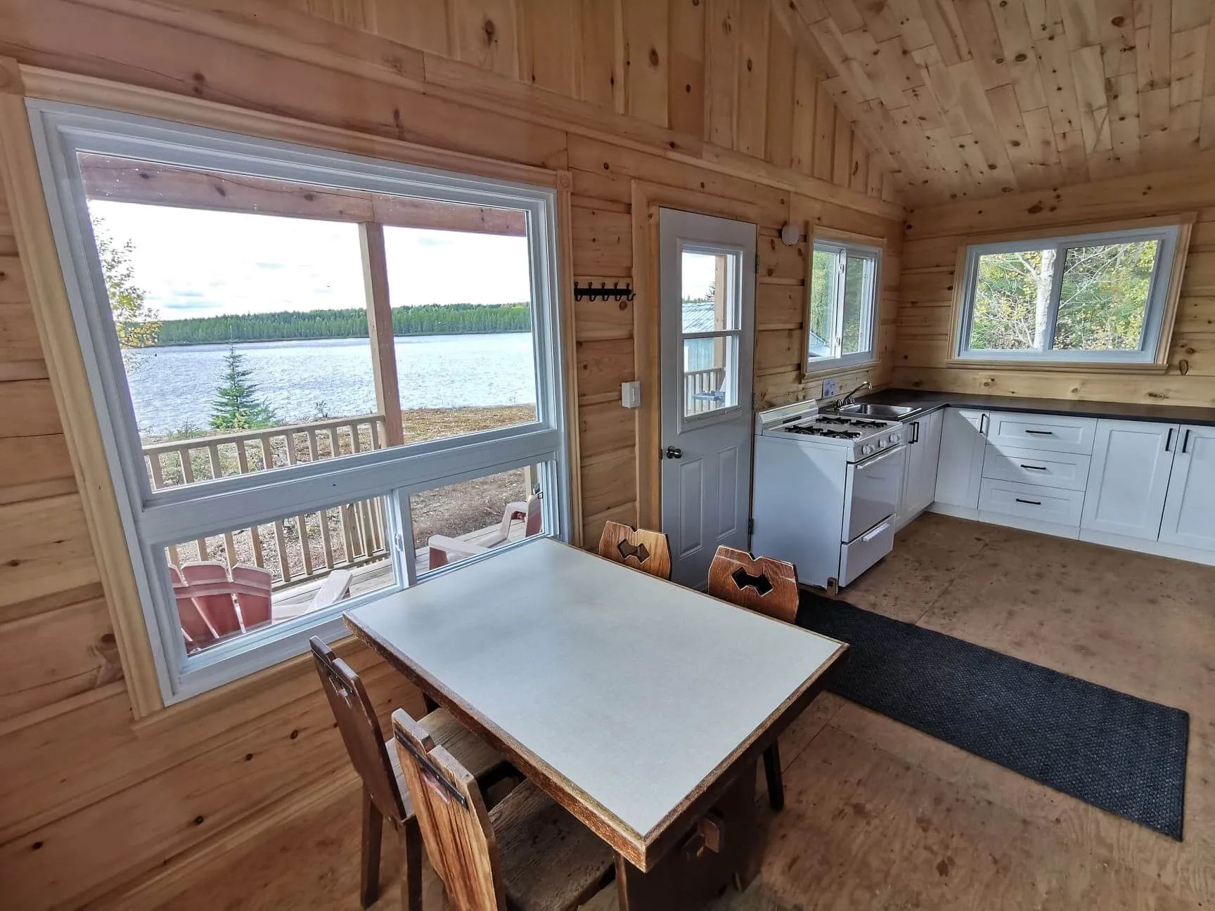 Vue de la cuisine et de la salle à manger ouverte sur la galerie et le lac depuis le chalet.
