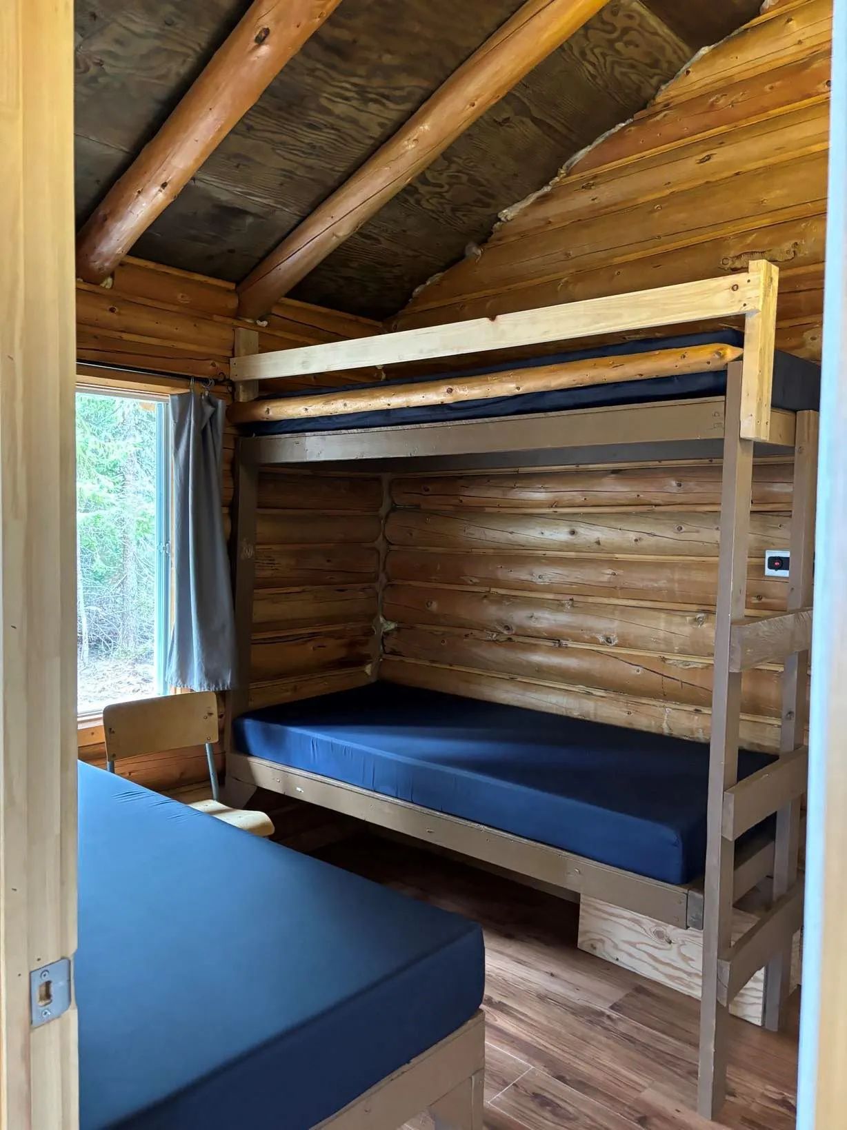 Cette chambre rustique du chalet comporte des lits superposés et un lit simple en bois rond.