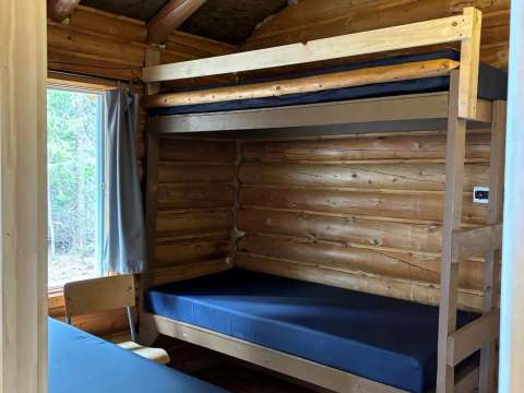 Cette chambre rustique du chalet comporte des lits superposés et un lit simple en bois rond.