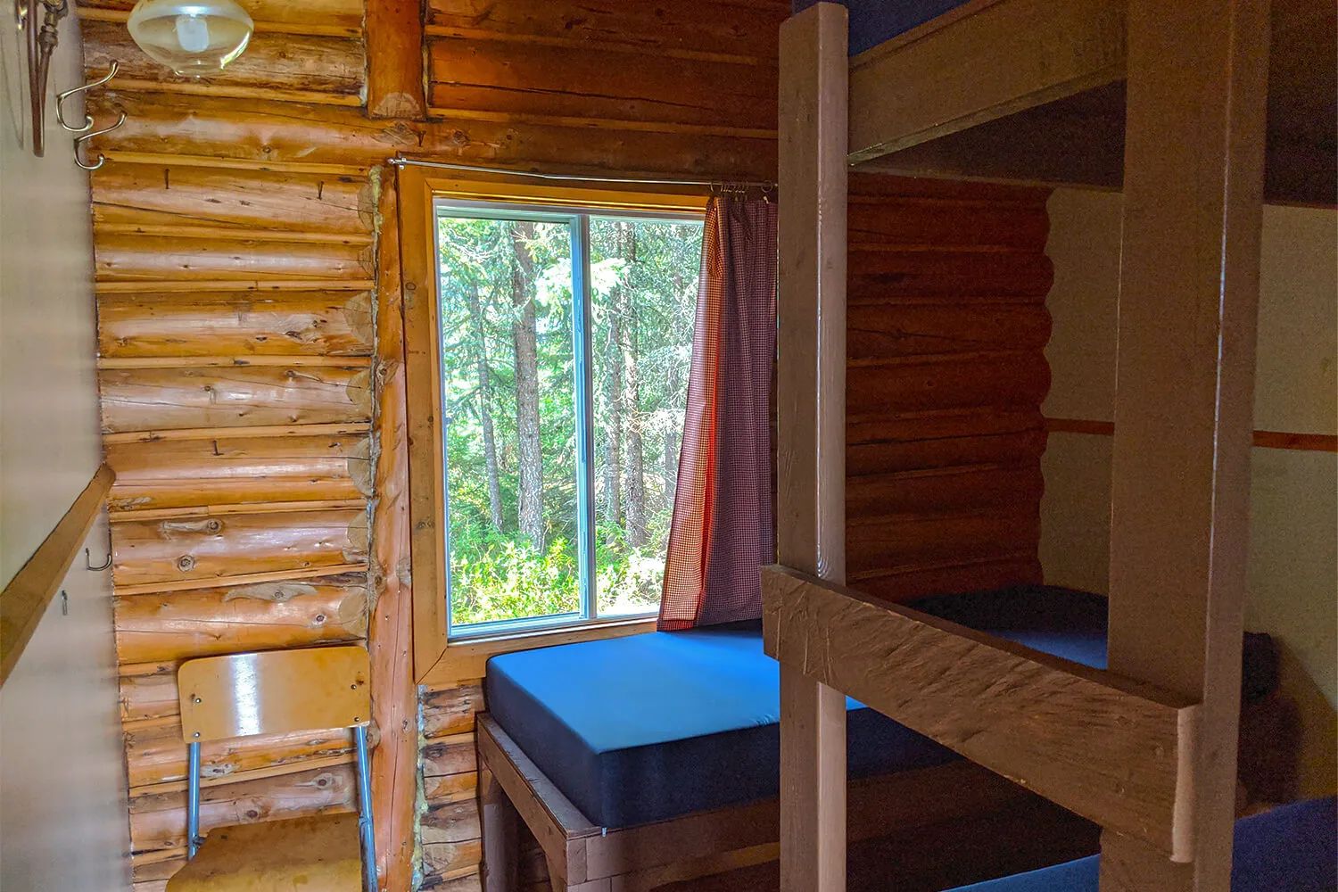 Cette chambre rustique avec murs en bois rond comprend des lits superposés et une fenêtre sur la forêt.