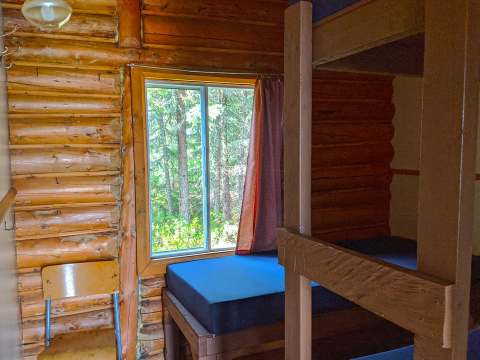 Cette chambre rustique avec murs en bois rond comprend des lits superposés et une fenêtre sur la forêt.
