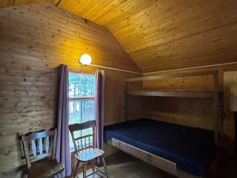 Cette chambre rustique du chalet comprend un lit superposé et deux chaises en bois.
