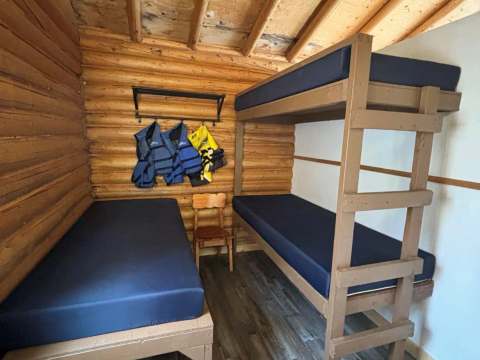 Cette chambre rustique comprend un lit simple et un lit superposé en bois.