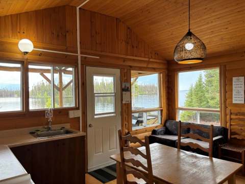 Vue de l'intérieur du chalet avec une table à manger et une vue sur le lac à travers les fenêtres.