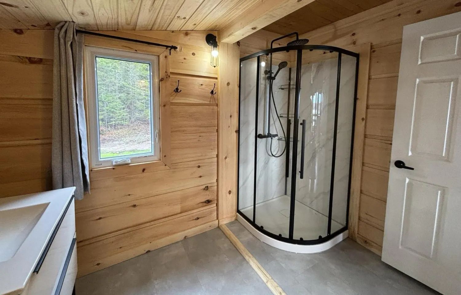 Cette salle de bain en bois du chalet comporte une douche moderne et une grande fenêtre.