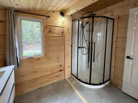 Cette salle de bain en bois du chalet comporte une douche moderne et une grande fenêtre.