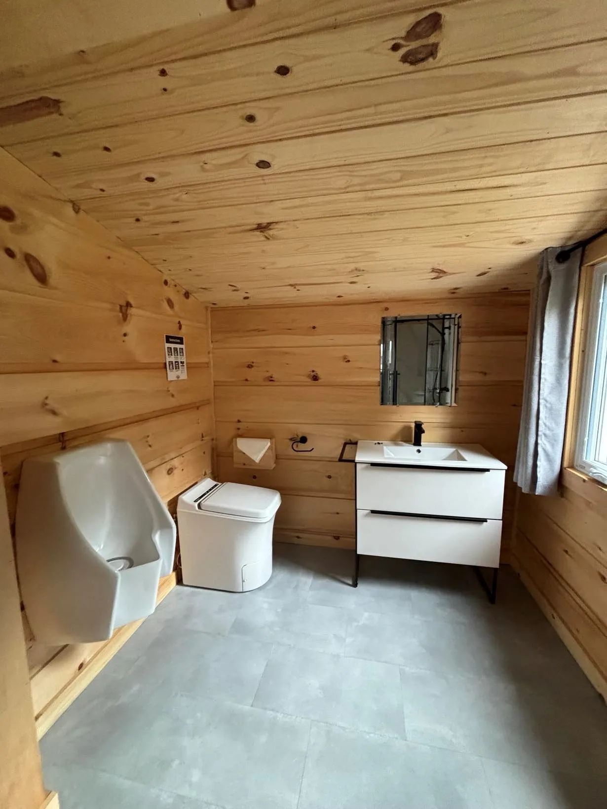 Vue de la salle de bain fonctionnelle avec toilette, urinoir et lavabo dans le chalet.