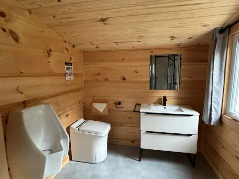 Vue de la salle de bain fonctionnelle avec toilette, urinoir et lavabo dans le chalet.