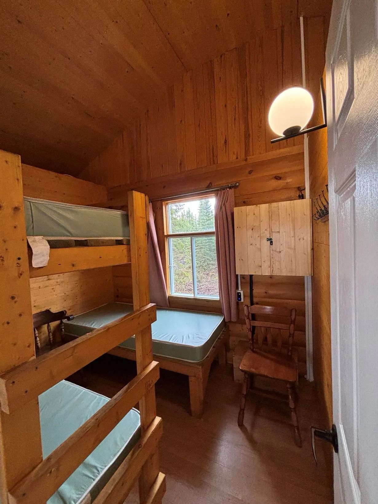 Cette chambre rustique comprend des lits superposés en bois et une fenêtre donnant sur la forêt.