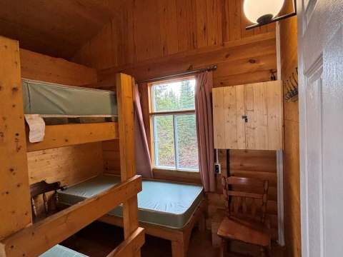 Cette chambre rustique comprend des lits superposés en bois et une fenêtre donnant sur la forêt.
