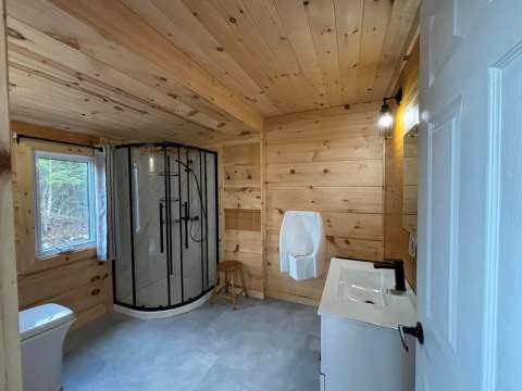 La salle de bain du chalet comporte une douche, un lavabo et un urinoir dans un décor en bois.
