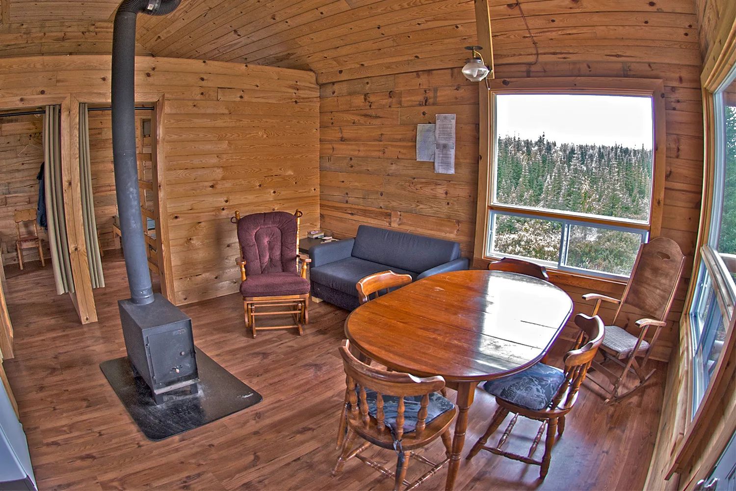 L'intérieur du chalet comprend un coin salon avec poêle à bois et une table à manger avec vue.