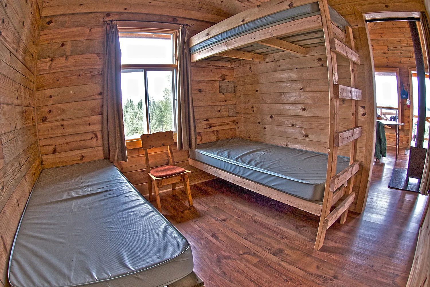 Cette chambre de chalet comprend un lit superposé et un lit simple avec des murs en bois.