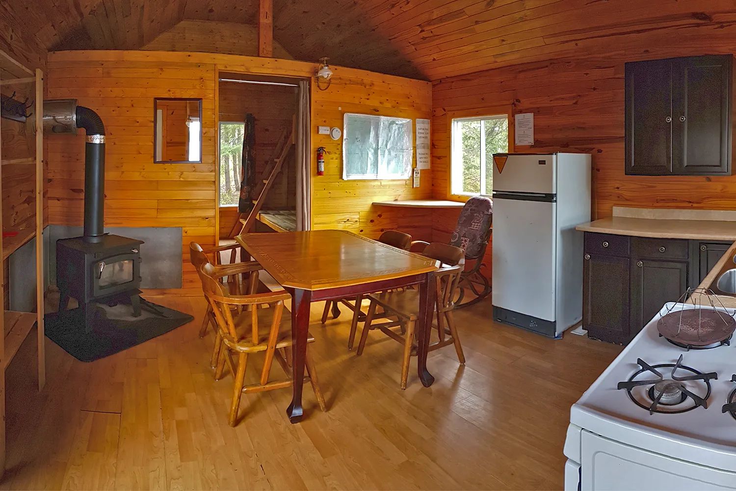 L'aire ouverte du chalet comprend une cuisine équipée, une table à manger et un poêle à bois.