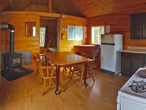 L'aire ouverte du chalet comprend une cuisine équipée, une table à manger et un poêle à bois.