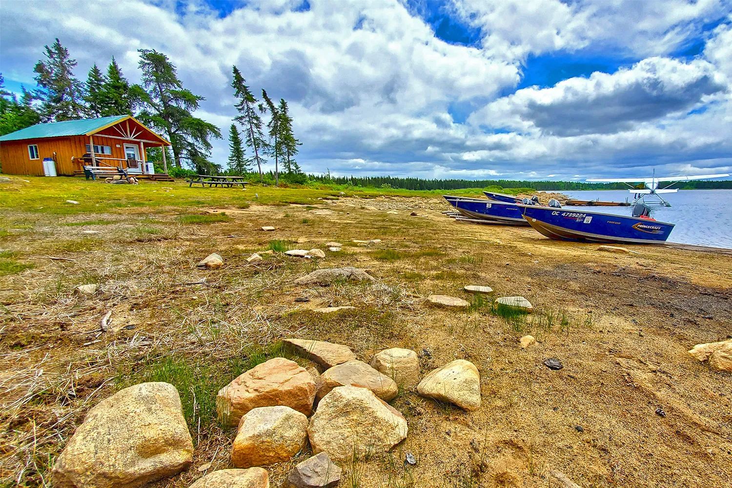 Le chalet se situe au bord de l'eau avec des embarcations et un hydravion à proximité.