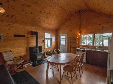 L'intérieur du chalet comprend une aire ouverte avec une cuisinette, une table à manger et un poêle.
