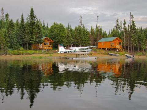 Vue sur les chalets en bois situés en bordure du lac avec un hydravion stationné sur la rive.
