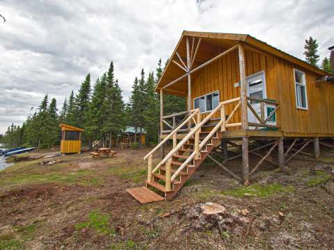 Vue extérieure du chalet en bois avec sa galerie et ses marches, situé près du rivage.