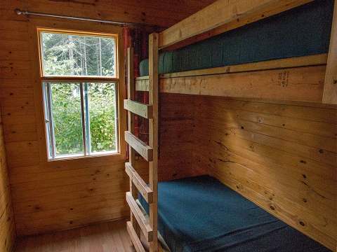 Cette chambre de chalet comprend un lit superposé en bois et une fenêtre donnant sur la forêt.