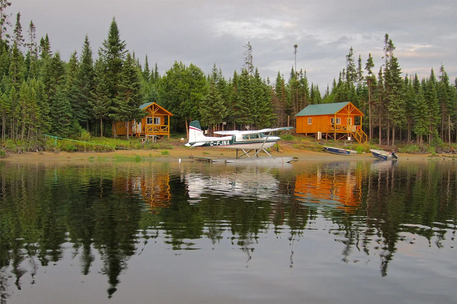 Vue sur les chalets en bois situés en bordure du lac avec un hydravion stationné sur la rive.