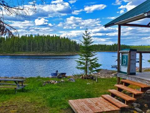 Vue sur le lac et la forêt depuis la galerie du chalet avec une table de pique-nique à proximité.