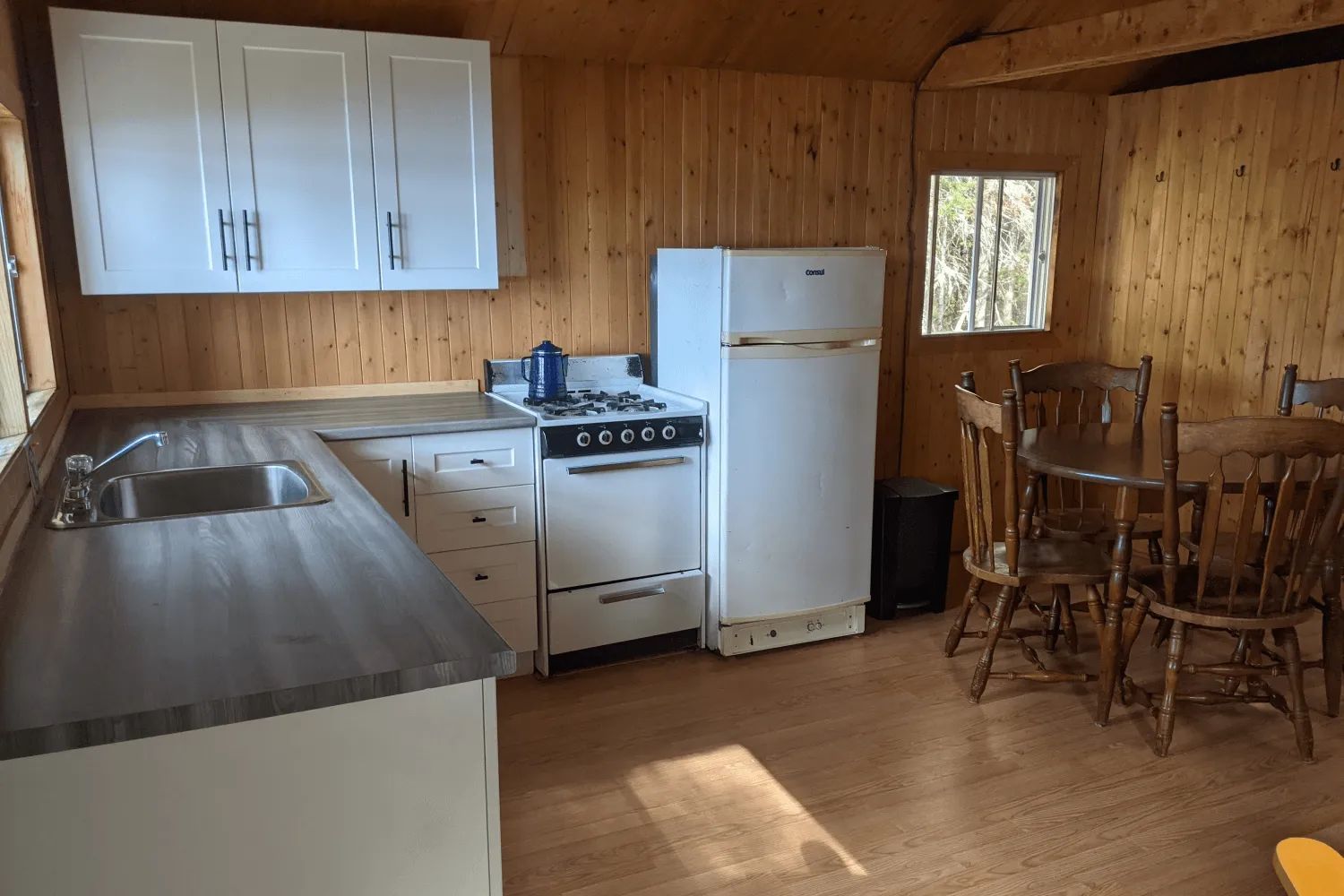 La cuisine fonctionnelle du chalet comprend une cuisinière, un réfrigérateur et une table à manger.