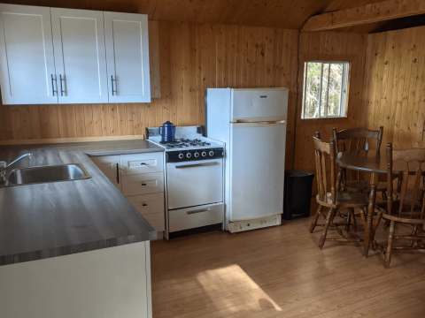 La cuisine fonctionnelle du chalet comprend une cuisinière, un réfrigérateur et une table à manger.