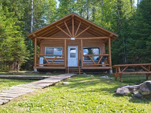 Vue extérieure du chalet en bois rond avec sa galerie et sa table à pique-nique.