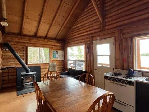 L'espace de vie du chalet comprend une table à manger, une cuisine fonctionnelle et un poêle à bois.
