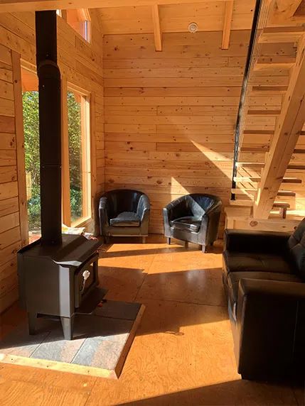 L'intérieur du chalet comprend un coin salon avec poêle à bois et escalier en bois.