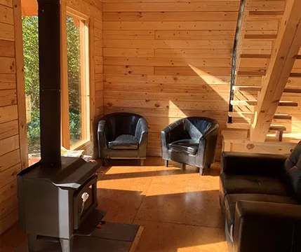 L'intérieur du chalet comprend un coin salon avec poêle à bois et escalier en bois.