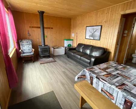 Le salon du chalet 2 comprend un canapé, un poêle à bois et une table à manger.