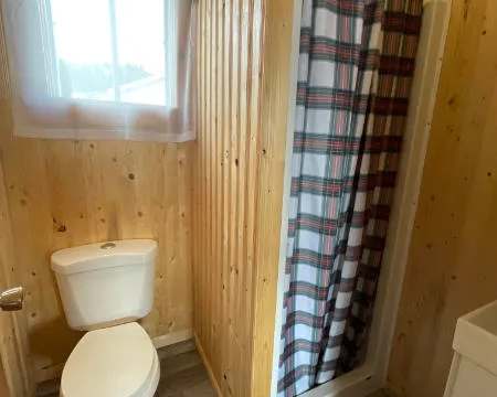 La salle de bain du chalet comprend une toilette et une douche avec rideau à carreaux.