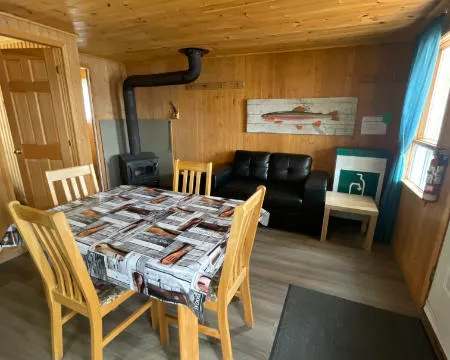 Espace de vie principal du chalet avec table à manger, divan et poêle à bois.