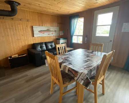 Coin repas et salon aménagés dans le chalet, avec murs lambrissés en bois.