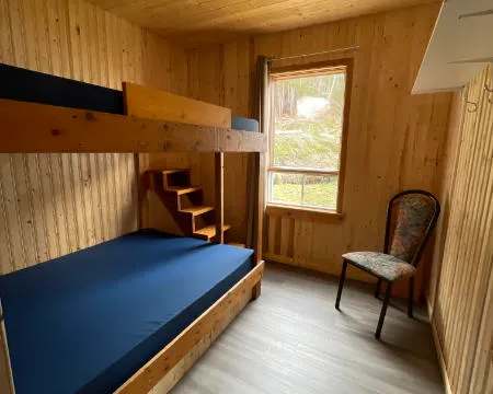 Cette chambre du chalet dispose d'un lit superposé en bois et d'une fenêtre donnant sur la forêt.