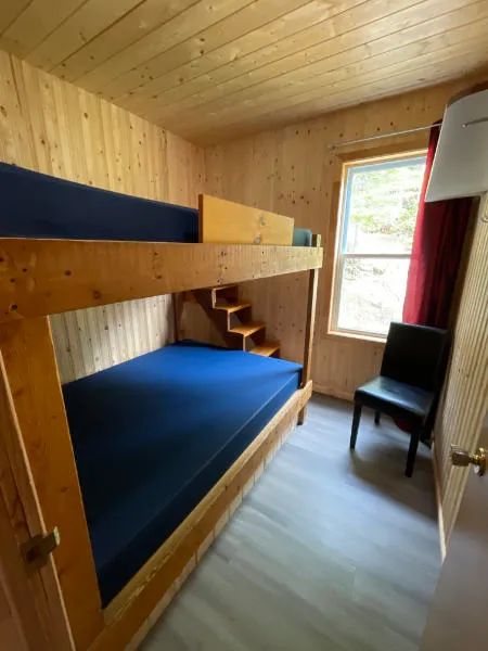 Cette chambre du chalet comprend un lit superposé en bois et une chaise à proximité de la fenêtre.