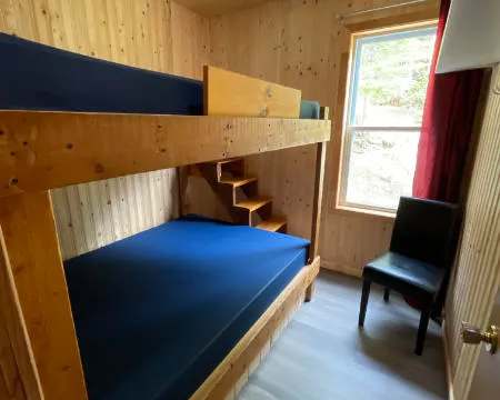 Cette chambre du chalet comprend un lit superposé en bois et une chaise à proximité de la fenêtre.