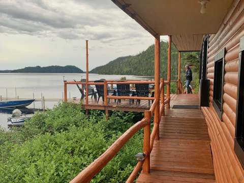 Vue sur le lac depuis la galerie extérieure du chalet avec terrasse et chaises.