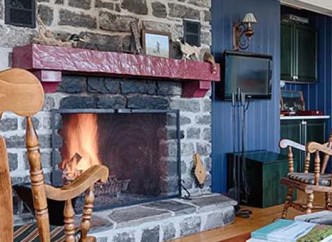 The main house living room features a stone fireplace and rocking chairs.