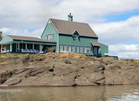 Overview of the main house situated on rocky terrain by the water.