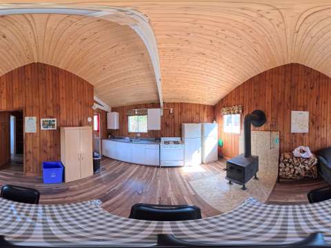 Panoramic view of the open area including the equipped kitchen, wood stove, and living room of the cabin.