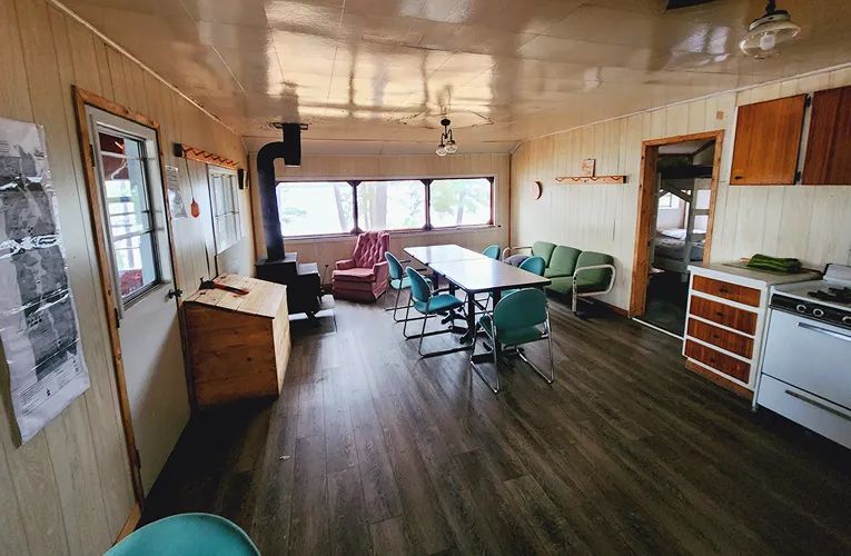 Vue d'ensemble de l'aire de vie principale du chalet comprenant une cuisine, une table et un poêle.