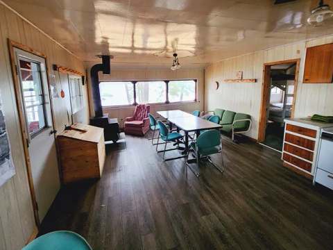 Vue d'ensemble de l'aire de vie principale du chalet comprenant une cuisine, une table et un poêle.