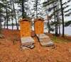 Deux toilettes sèches extérieures en bois situées près de la forêt et du lac.